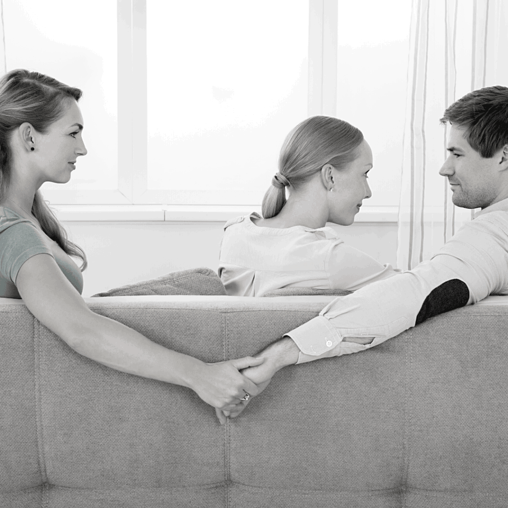 2 woman and a man acting a betrayal by holding the other woman's hand while facing his partner