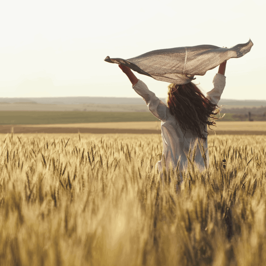 woman in the middle of field holding a scarf up high