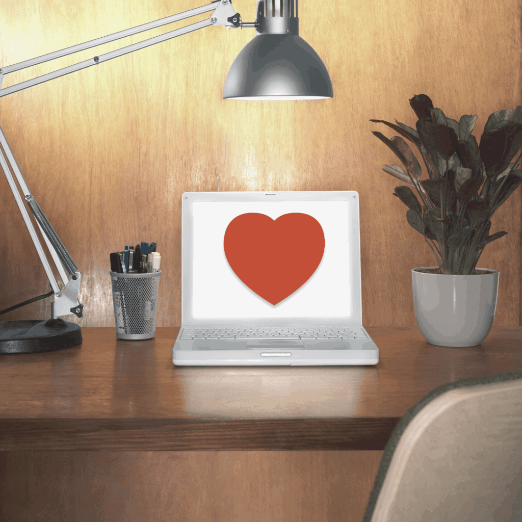 a laptop online with a heart on top of desk focused by a lamp