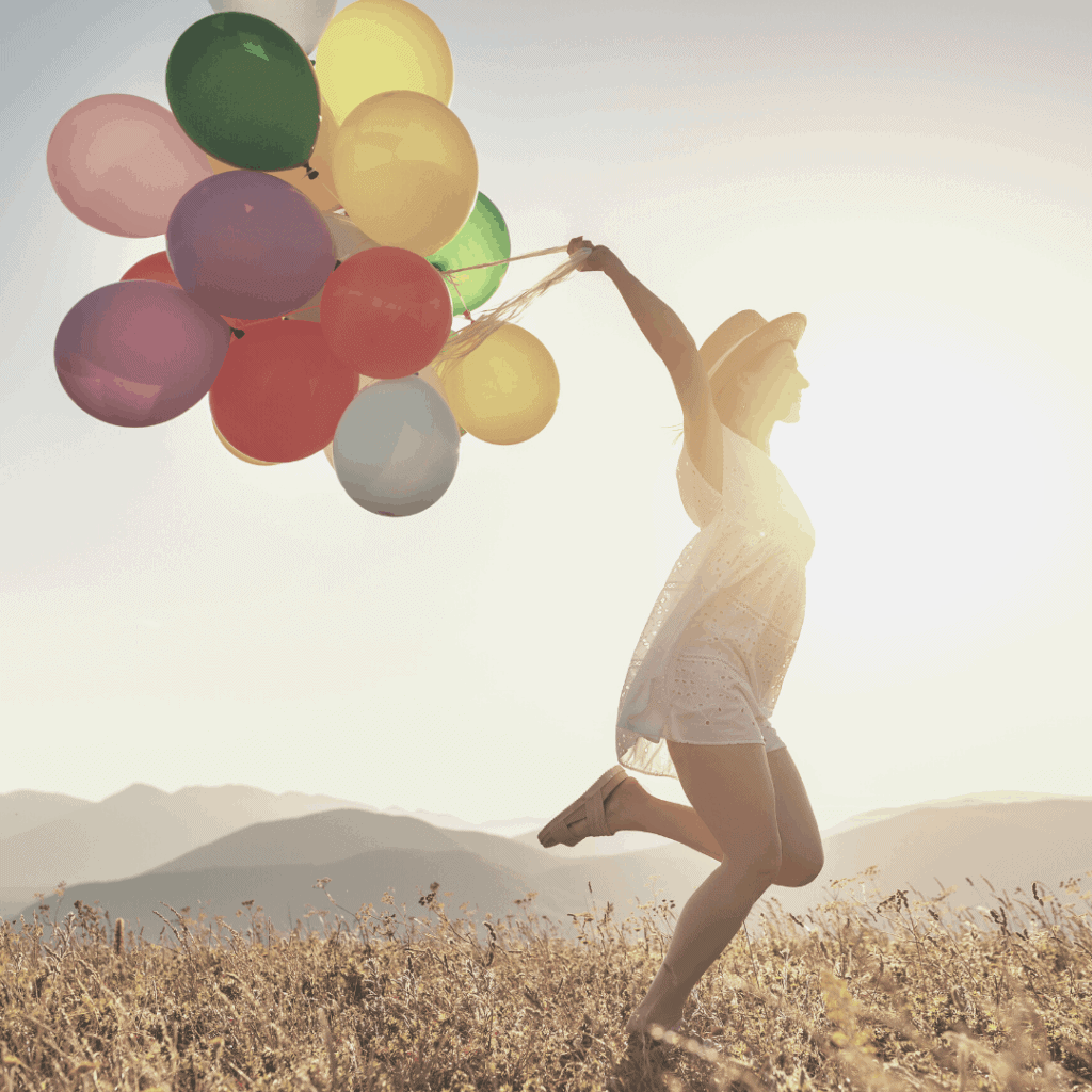 woman holding colorful balloons in front a sunrise