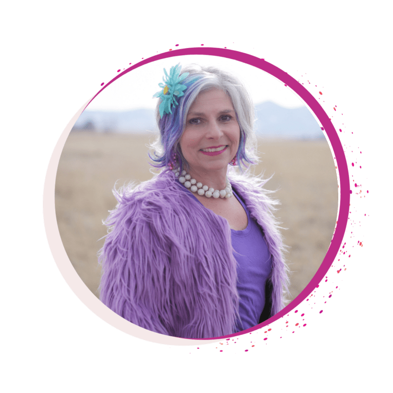 Macy Matarazzo smiling wearing a purple fur coat on top of a purple shirt, white big beads necklace and a blue flower on her hair