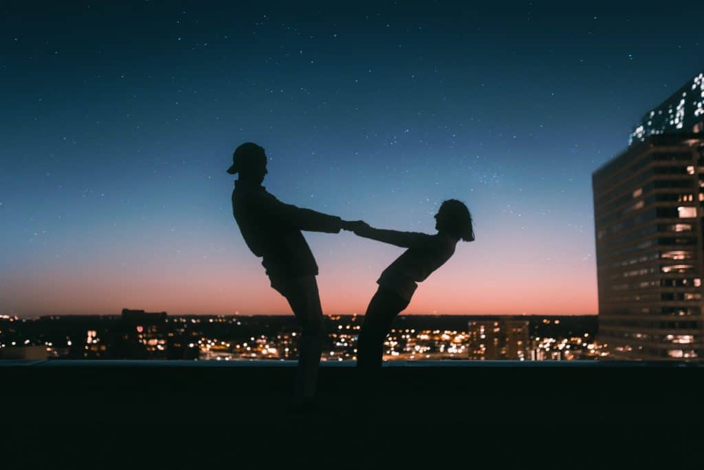 couples on top of a building holding each others hand in front of a city lights view