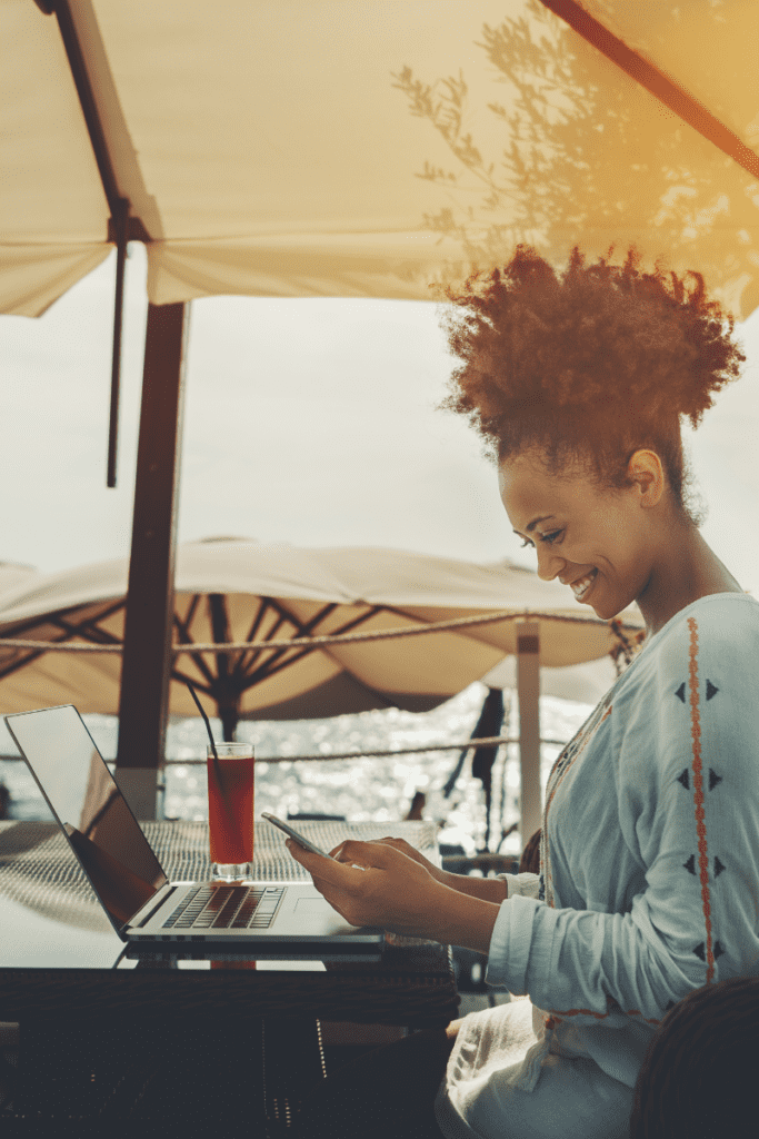 smiling Afro girl in nearshore bar with laptop and smartphone