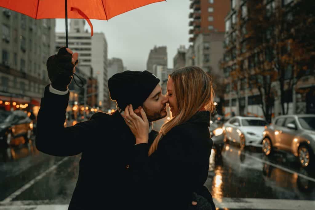 man holding a red umbrella about to kiss a woman