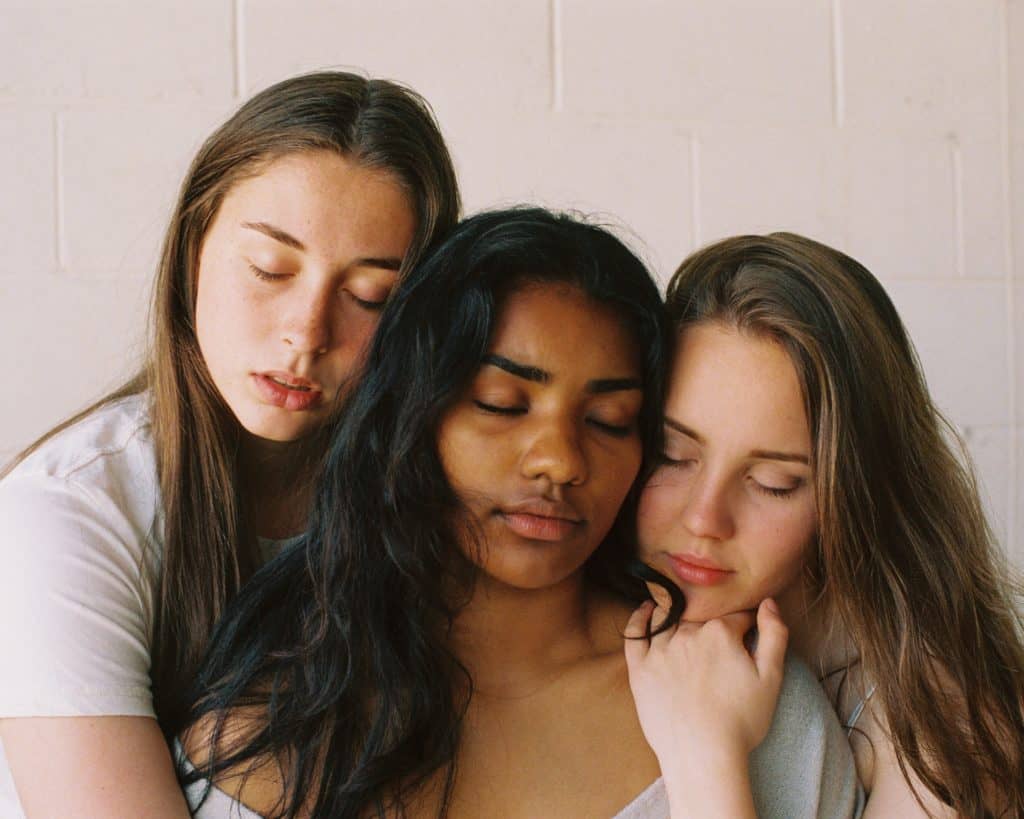 2 white woman hugging a black woman with their eyes closed