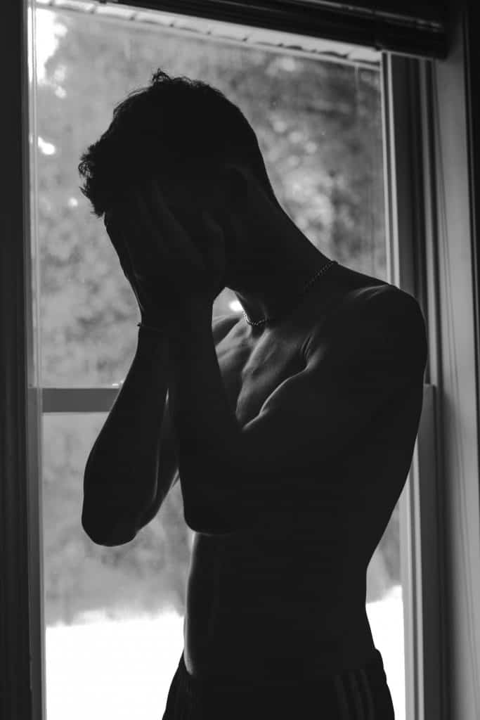a black and white image of a man half naked looking sad by covering his face