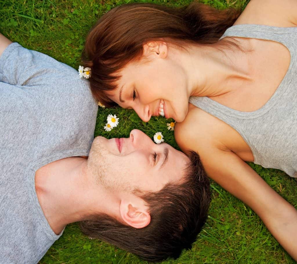 a couple lying on the green grass facing each other with their heads upside down