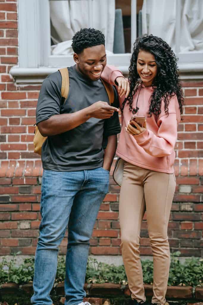 a black man and woman smiling together while looking at the woman's mobile phone