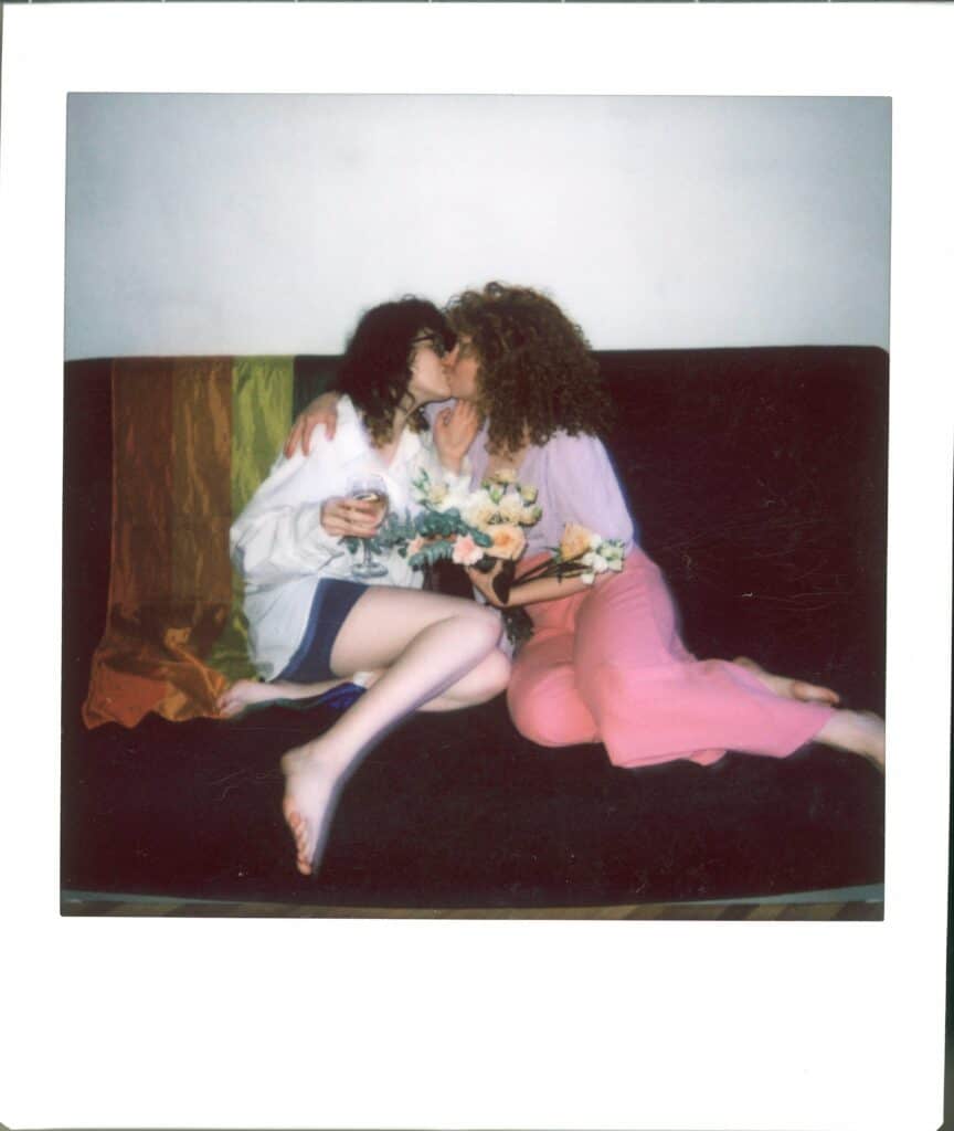 female women kissing each other while holding a bouquet of flowers on a couch