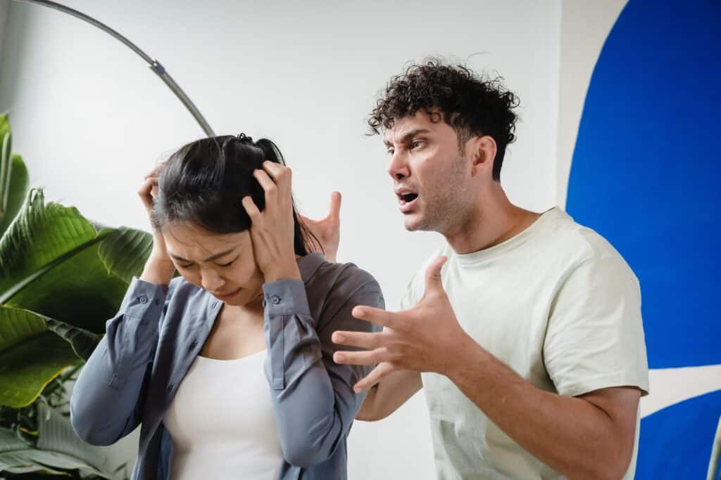 a man screaming at his woman partner while the woman is covering her ears and is in fear