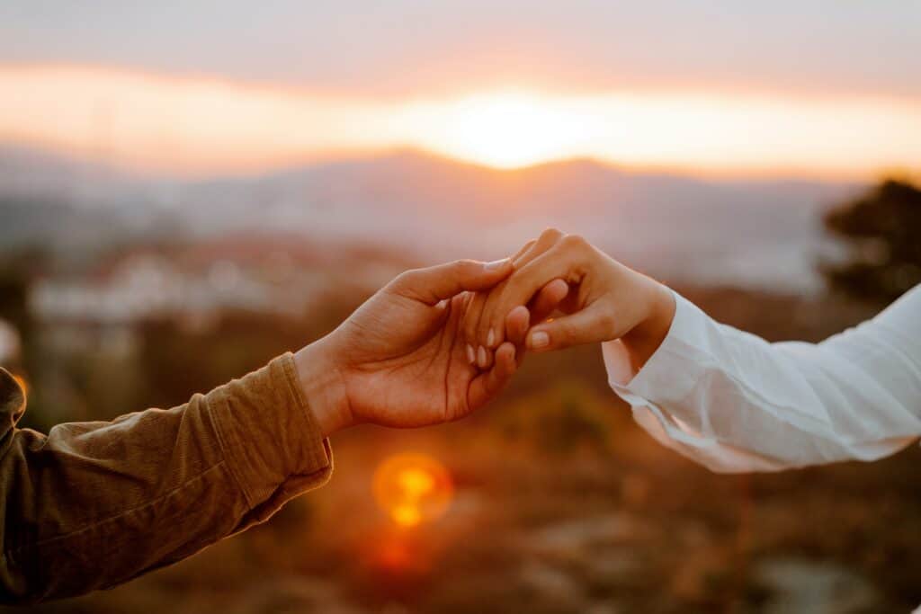 a photo of a man and woman's hand holding each other in front of a beautiful sunset