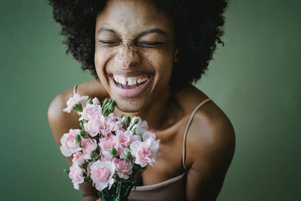 a beautiful photograph of a black woman with a big smile while holding a bouquet of pink flowers