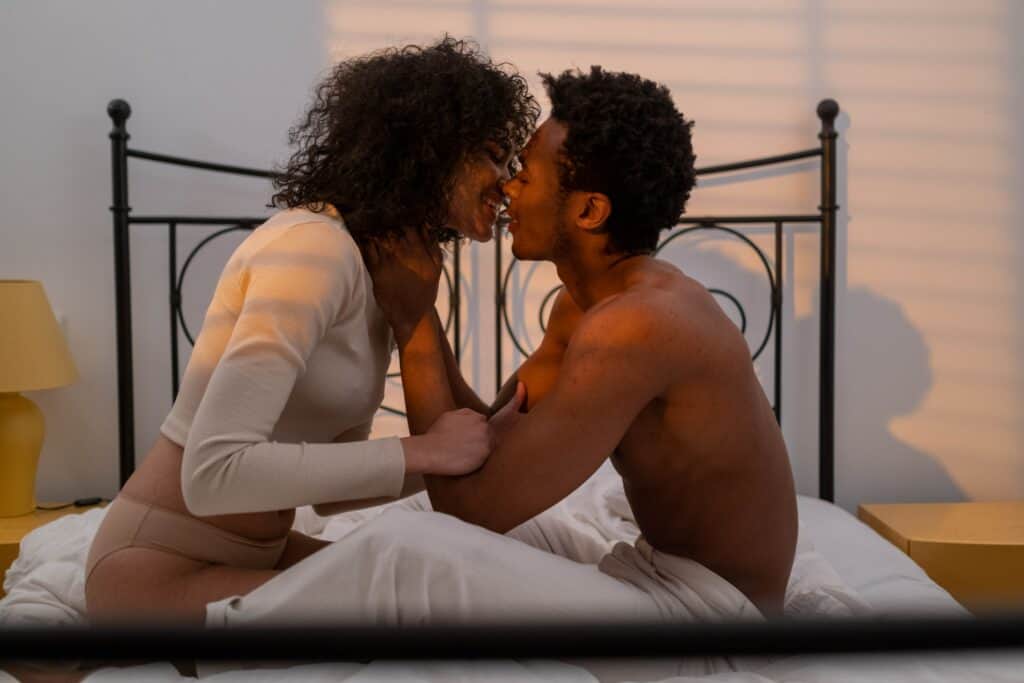 a photo of a man and woman on the bed, sitting down facing each other and about to kiss