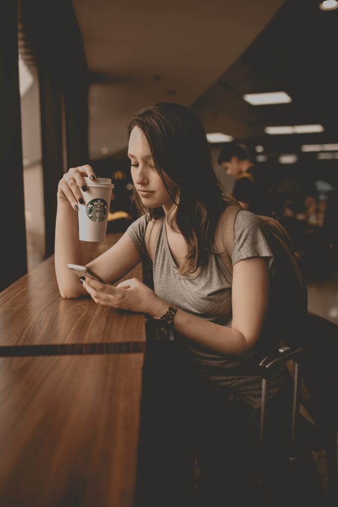 a greyscale photo of a woman checking her phone while holding a cup of coffee